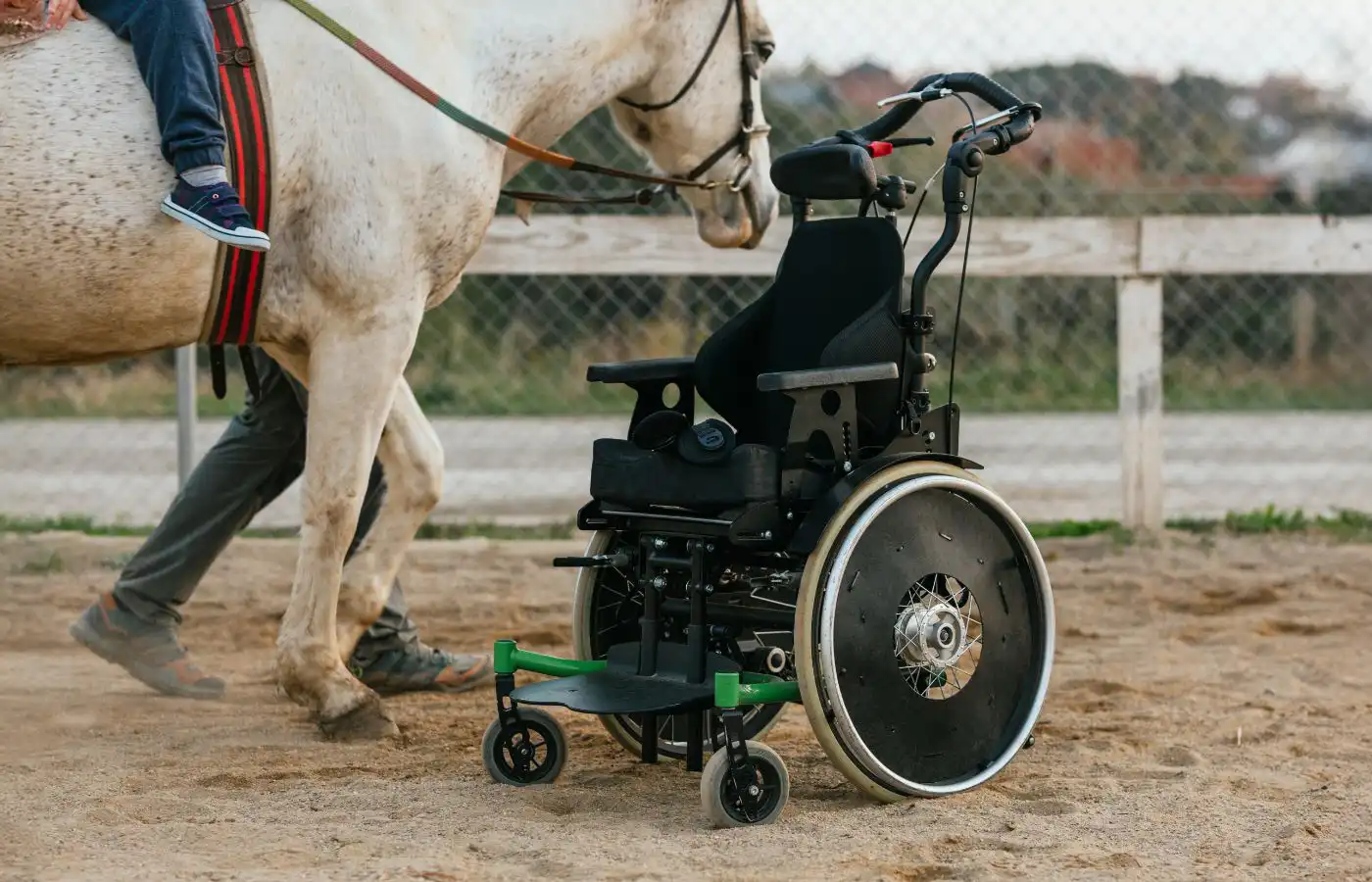 Fauteuil roulant en premier plan et enfant montant un cheval dans un cadre d'équithérapie, illustrant les bienfaits de la thérapie pour les personnes à mobilité réduite.